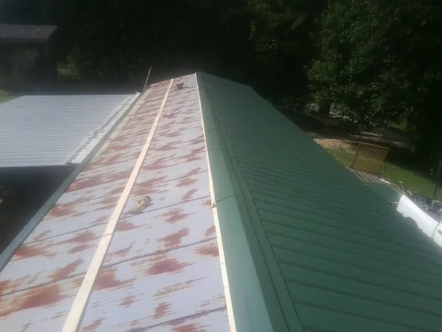 Old rusted panels beside newly installed green metal roofing — Wind Damage Roof Repair by Roofing Brothers in Bunker Hill