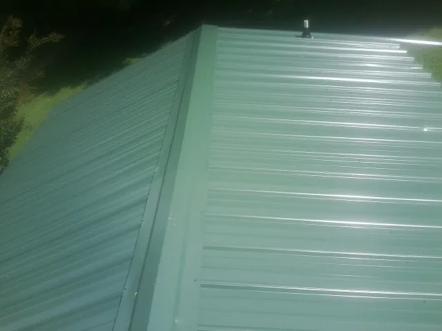 New green metal panels meeting at the ridge of a roof — Flat Roof Repair work by our crew in Bunker Hill