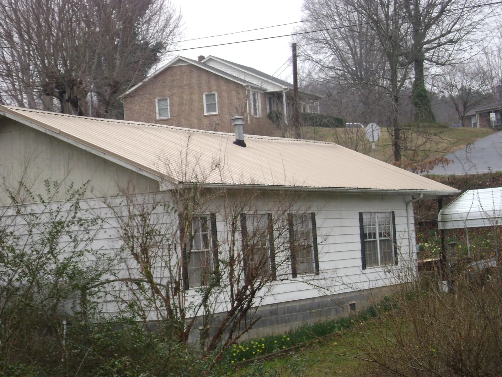 Tan metal roof on a white sided house set into a hillside — Commercial Roofing by Roofing Brothers in Bunker Hill